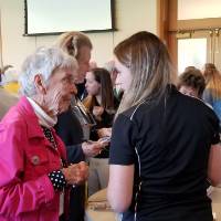 An older woman talks to a younger woman, while a young woman smiles talking to a man and woman